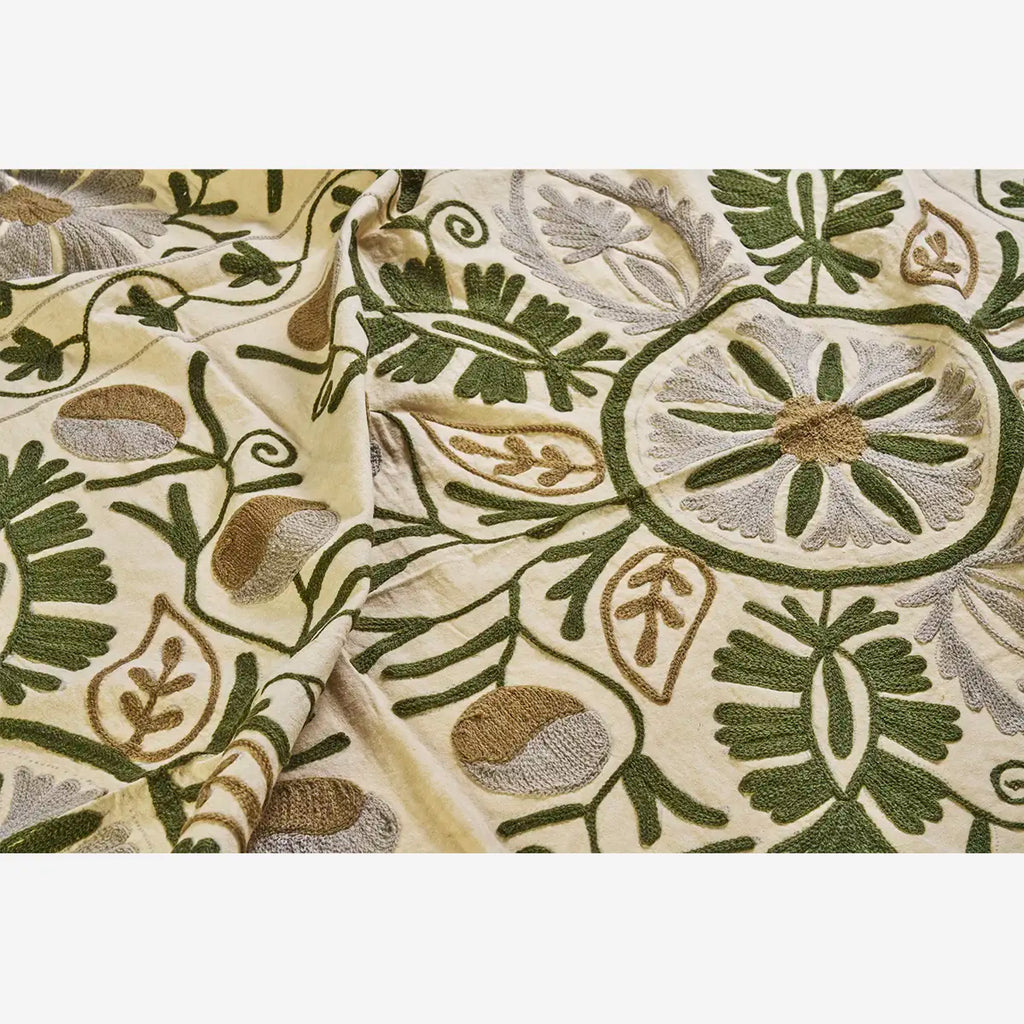 Embroidered fabric with green and grey floral patterns on a beige background