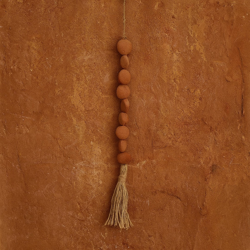 String of terracotta beads with a tassel on a textured brown background