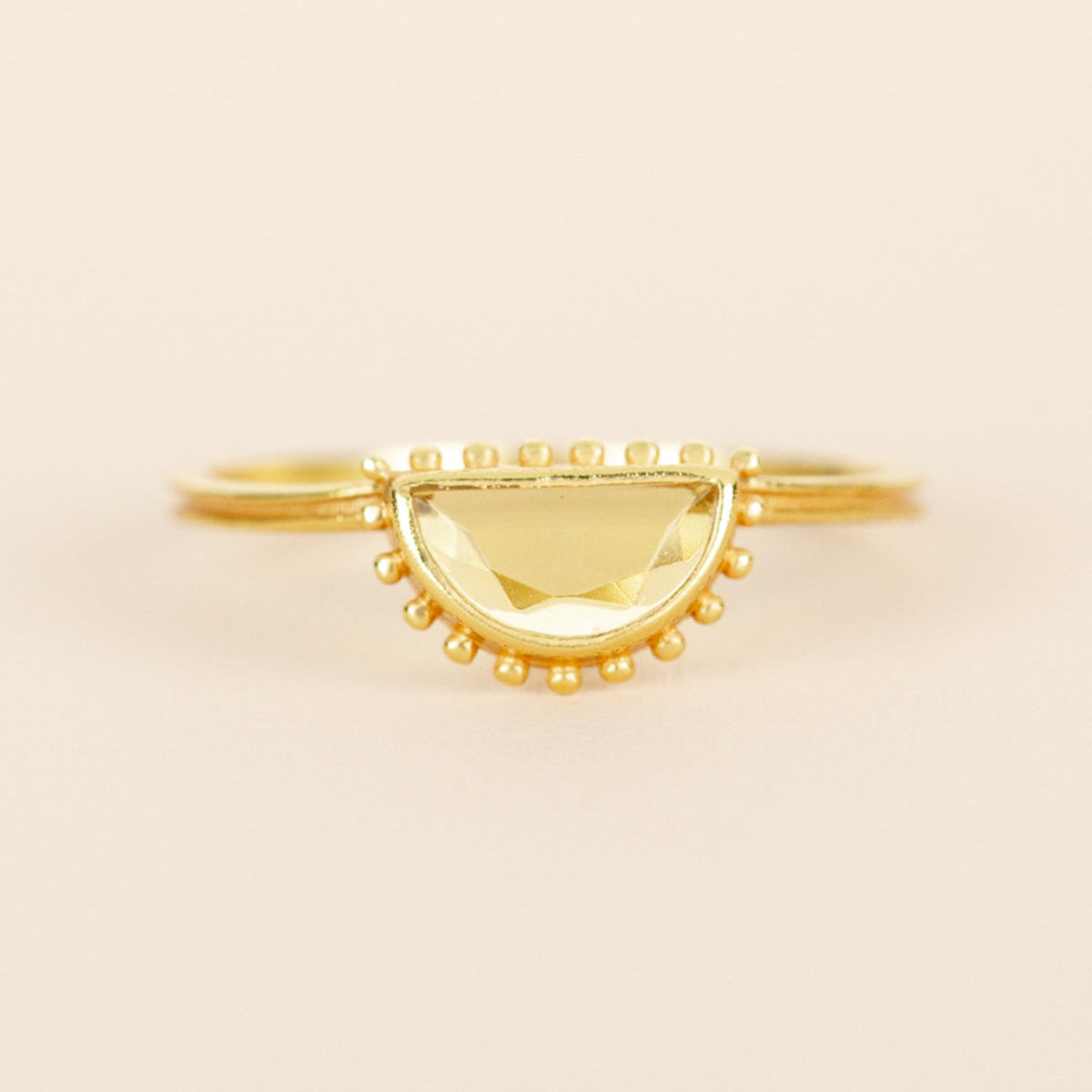 A gold semi-circular ring with a faceted yellow center and small gold bead accents along the curved top.