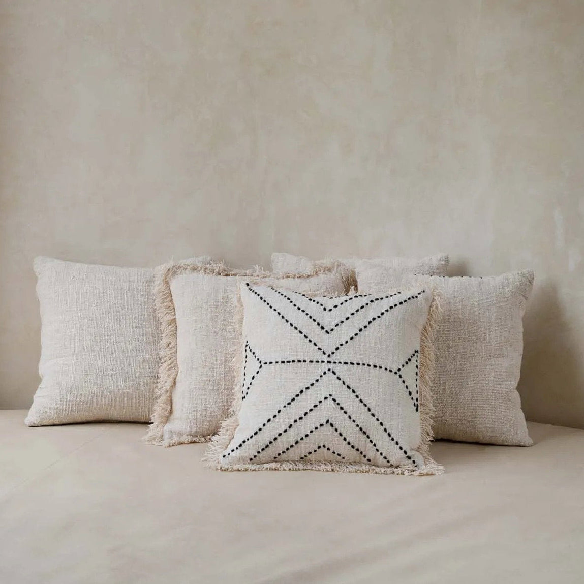 Beige pillows on a bed with a woven pendant light above against a beige wall.