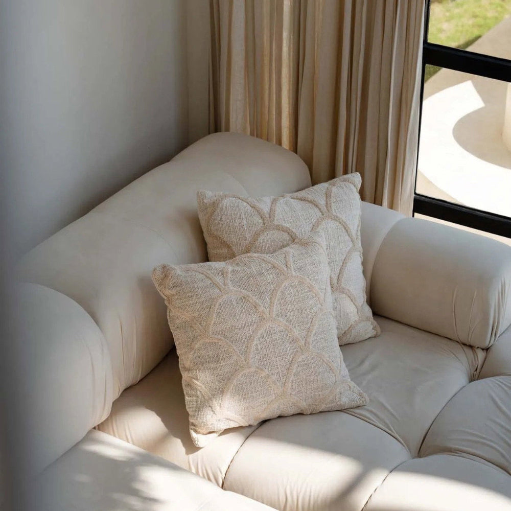 Beige sofa with patterned cushions in a room with curtains and a window.