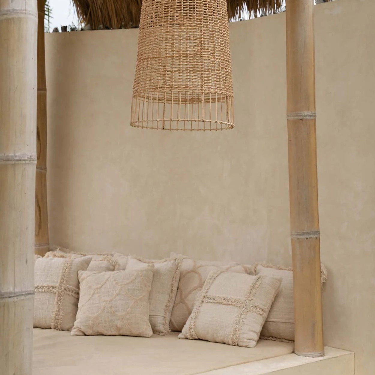 Nestled corner with woven wicker chair, textured pillows, and a hanging wicker lamp in a natural setting.