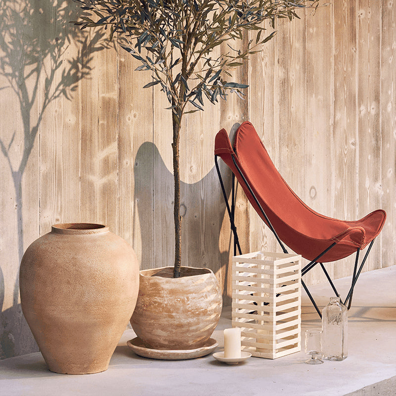 Decorative setting with a terracotta chair, potted plant, and vases against a wooden wall.