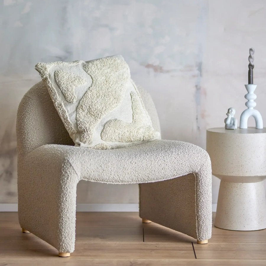 Beige armchair with textured cushions in a room with a lamp and decorative items.