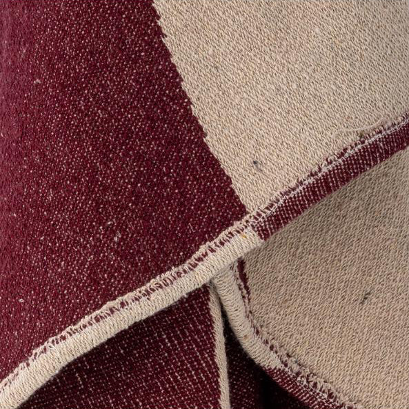 Un gros plan d’un textile tissé à motif quadrillé, dans des tons de bordeaux profond et de beige chaleureux, montrant la texture du tissu et les bords cousus.