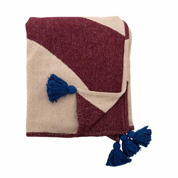 Une couverture tissée pliée, à motif géométrique bordeaux profond et crème, avec des pompons bleu foncé aux coins