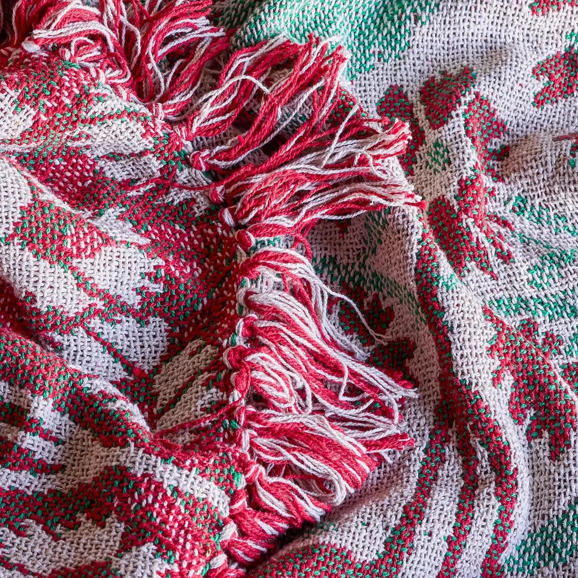 A close-up of a woven blanket with red and green patterned stripes and fringed tassels