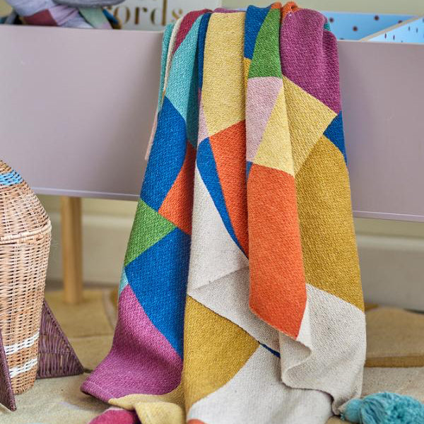 Colorful geometric-patterned blanket draped over a chair with a neutral background
