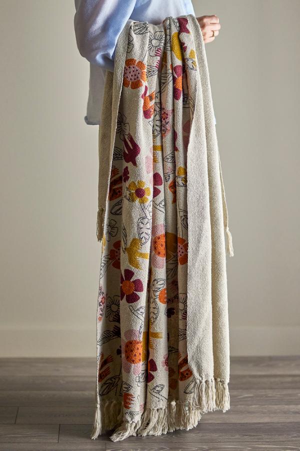 Person holding a floral-patterned blanket with tassels