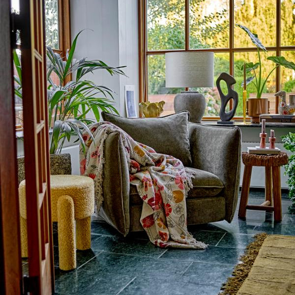 Living room with a gray armchair, colorful blanket, and large windows.
