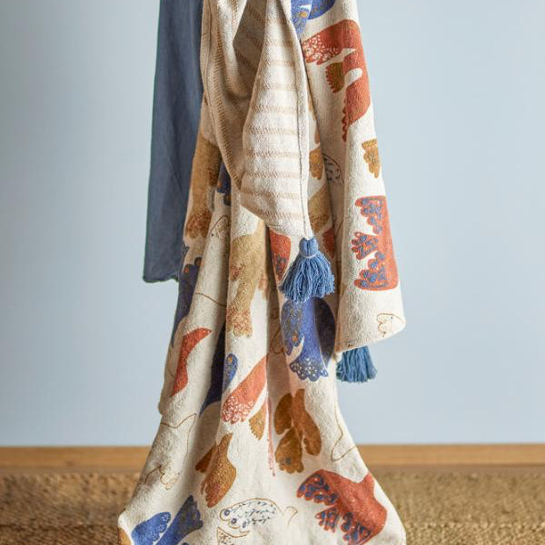 Person holding a bird-patterned blanket with tassels 