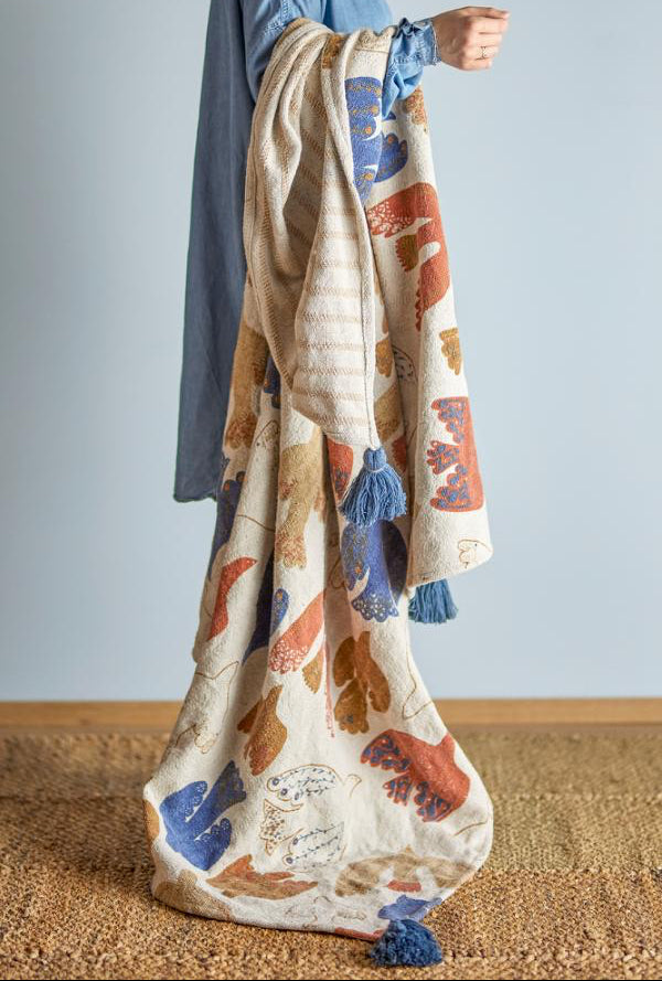 Person holding a bird-patterned blanket with tassels 