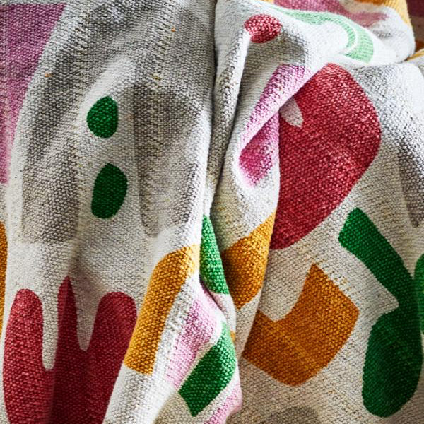 A close-up of a textured fabric with a colorful abstract pattern on a light beige background.