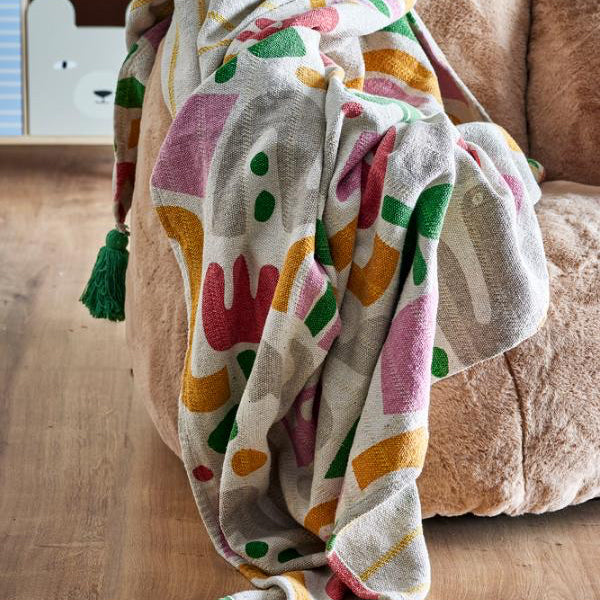 A multicolor patterned throw blanket with green tassels draped over a brown armchair on a wooden floor.