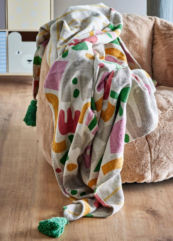 A multicolor patterned throw blanket with green tassels draped over a brown armchair on a wooden floor.