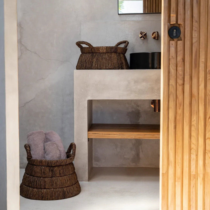 Bathroom interior with concrete vanity, wicker baskets, and wooden door.