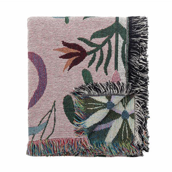 A folded woven throw blanket with a dusty pink background and a multicolor botanical pattern, featuring dark green leaves, white flowers, and black-and-white fringed edges.