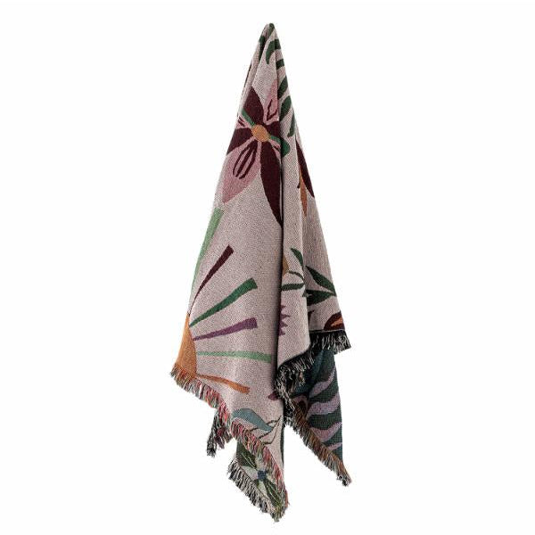 A patterned throw blanket with fringed edges, featuring a botanical design in shades of burgundy, green, orange, and gray on a light beige background, shown hanging against a plain white background.