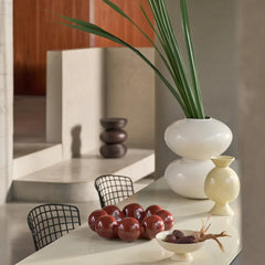 White vase with green plant with decorative items in a modern interior setting.
