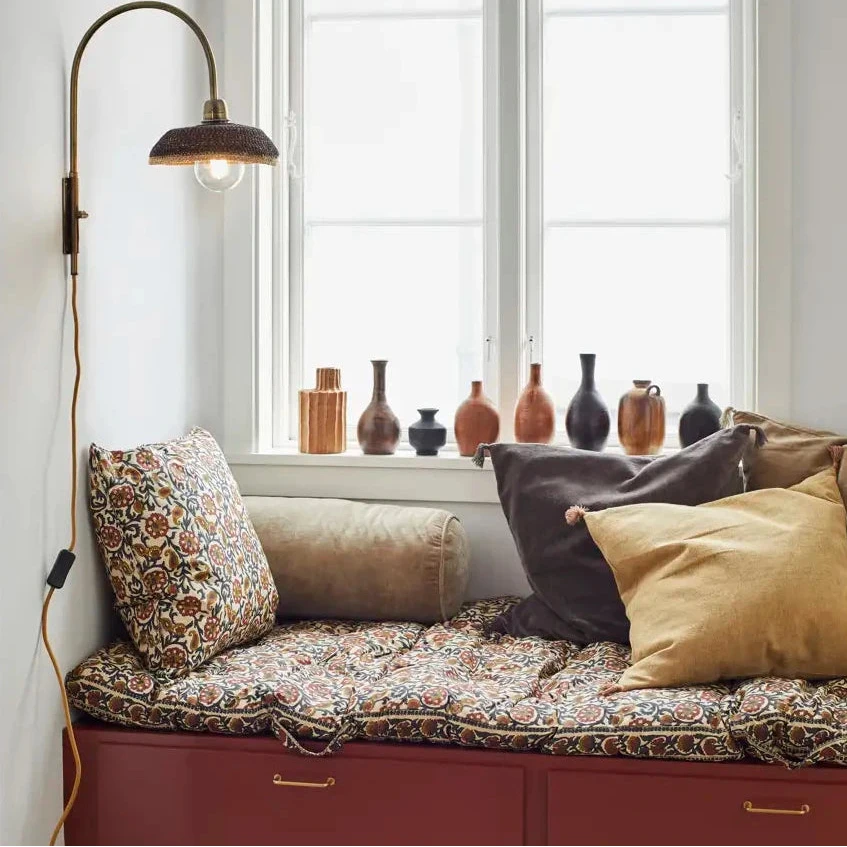 Window seat with cushions and a lamp in a room with decorative vases on the windowsill.