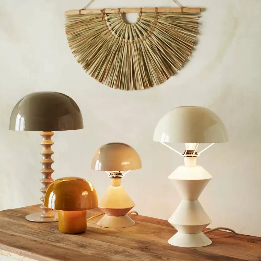 Collection of decorative lamps on a wooden table with a woven wall art piece above.