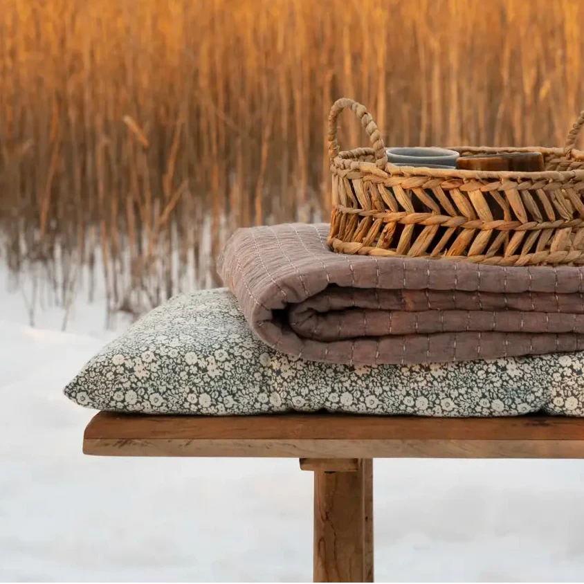 Wicker basket and folded blankets on a wooden bench with bench cushion
