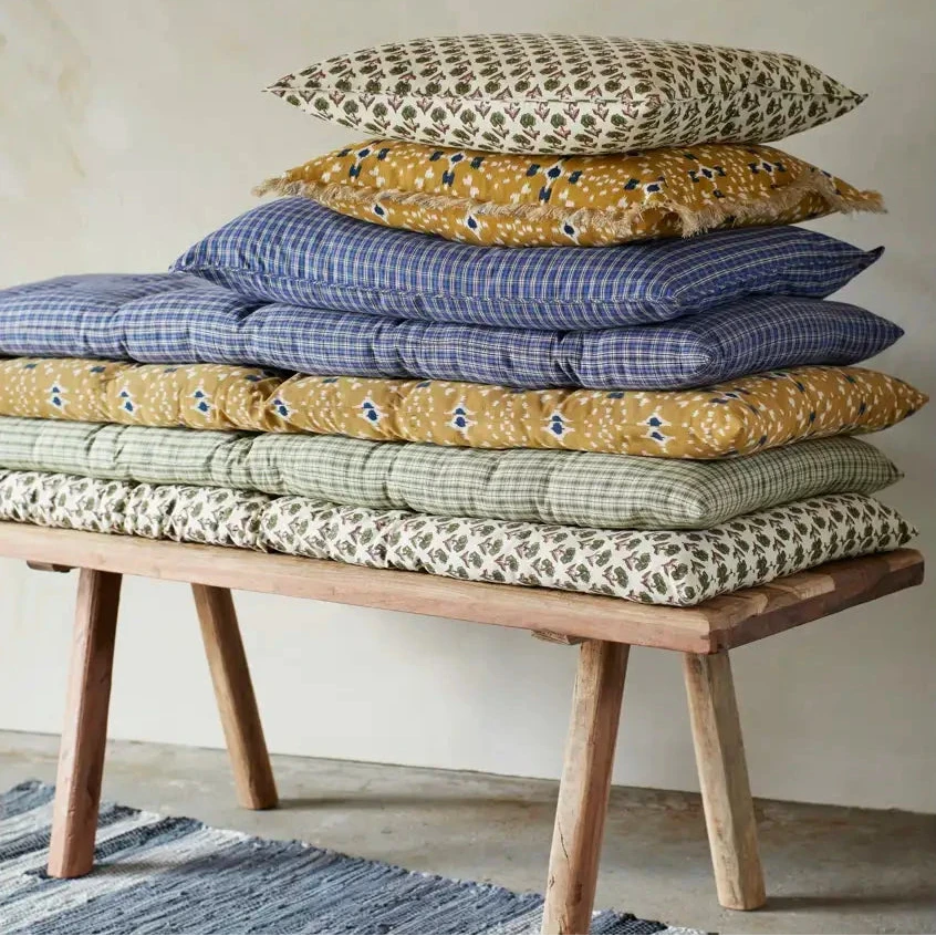 Stack of patterned cushions on a wooden bench by Madam Stoltz