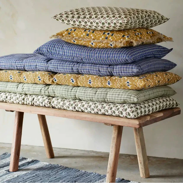 Stack of patterned cushions on a wooden bench by Madam Stoltz
