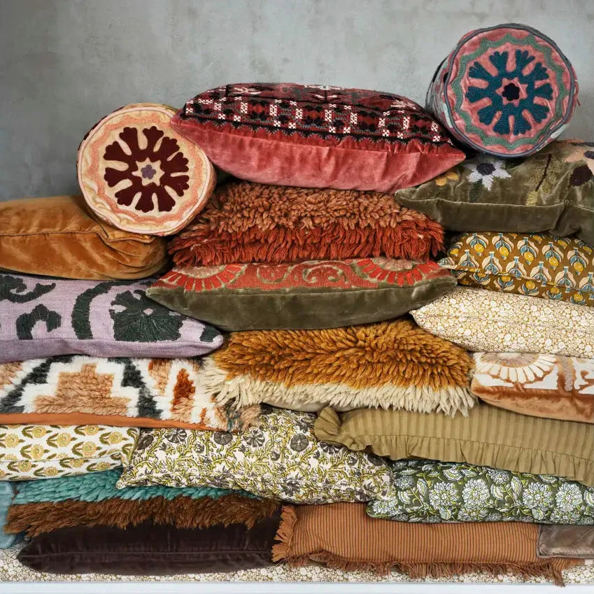 A stacked collection of decorative throw pillows and textured cushions in assorted earthy tones, patterns, and fabrics by Madam Stoltz