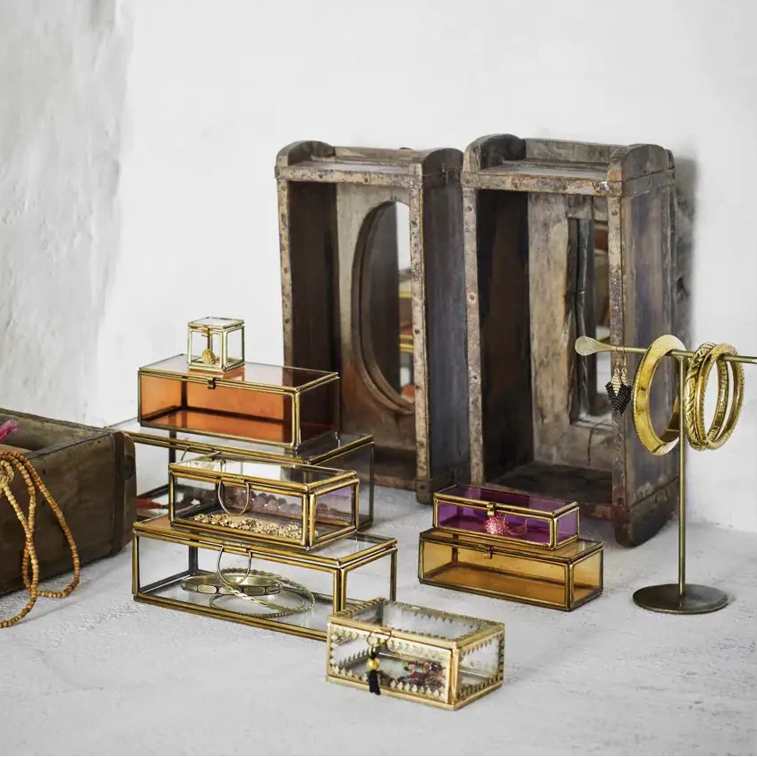 A styled collection of vintage jewelry boxes and display stands, including distressed wood crates with mirrored fronts, gold-framed glass boxes, and a gold ring stand