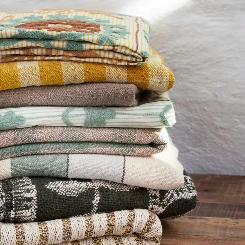 Stack of folded blankets with various patterns and colors on a wooden surface.