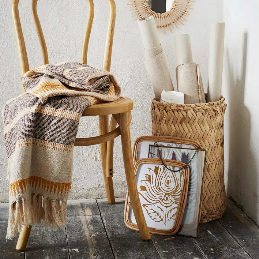 A styled interior corner by Madam Stoltz with a light wood bentwood chair draped with a beige, brown, and mustard throw blanket. 