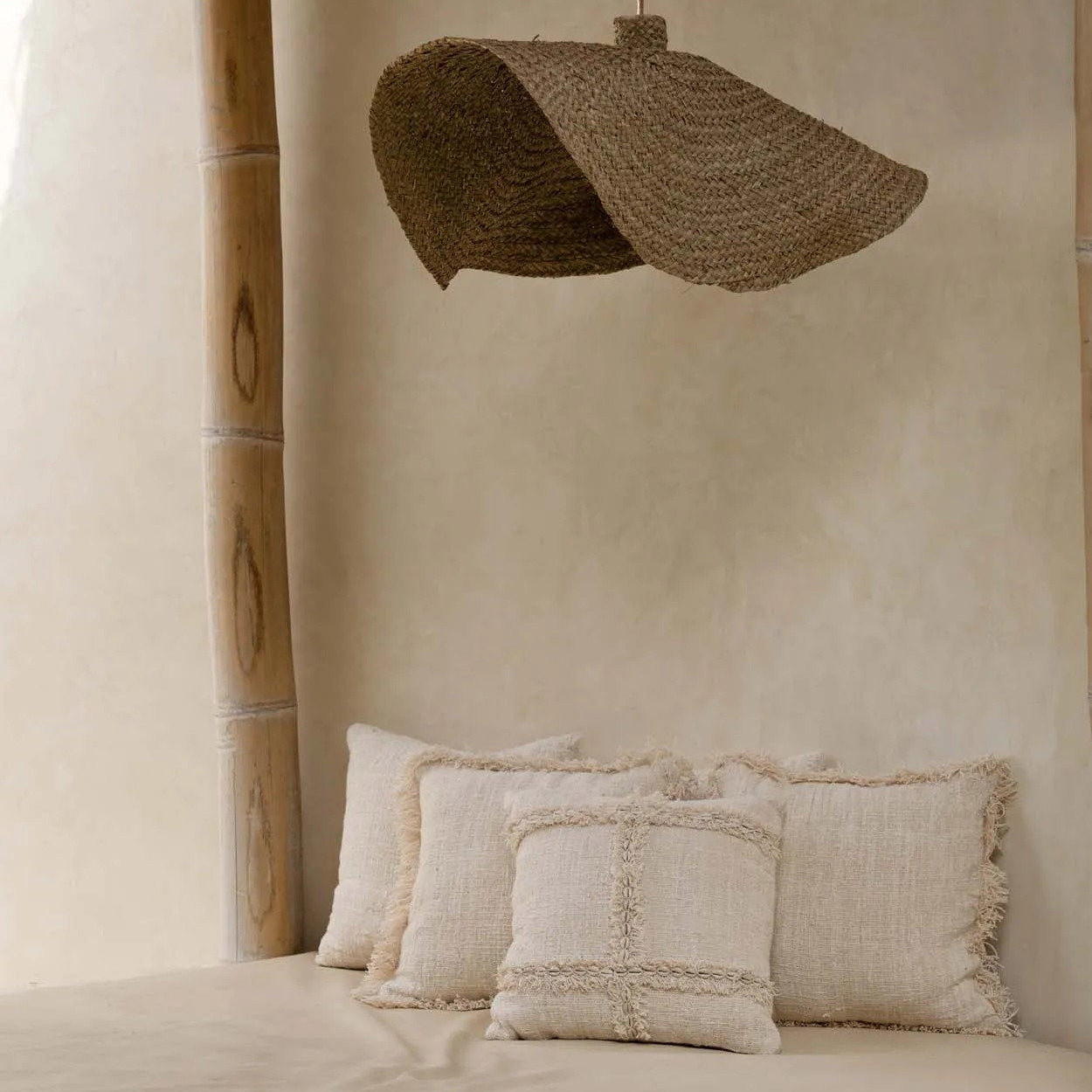 Beige interior with cushions on a bench and a woven lampshade hanging from a thatched roof.