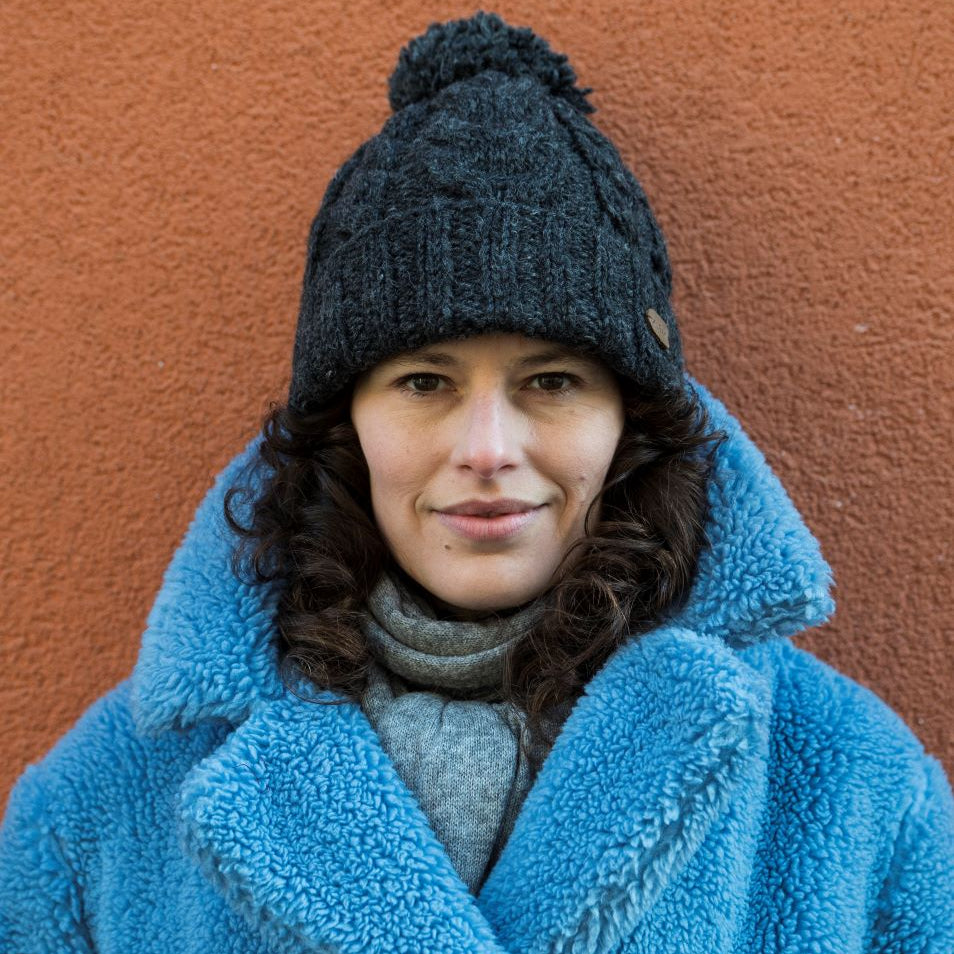 A woman wearing a dark gray cable-knit beanie with a pom-pom 