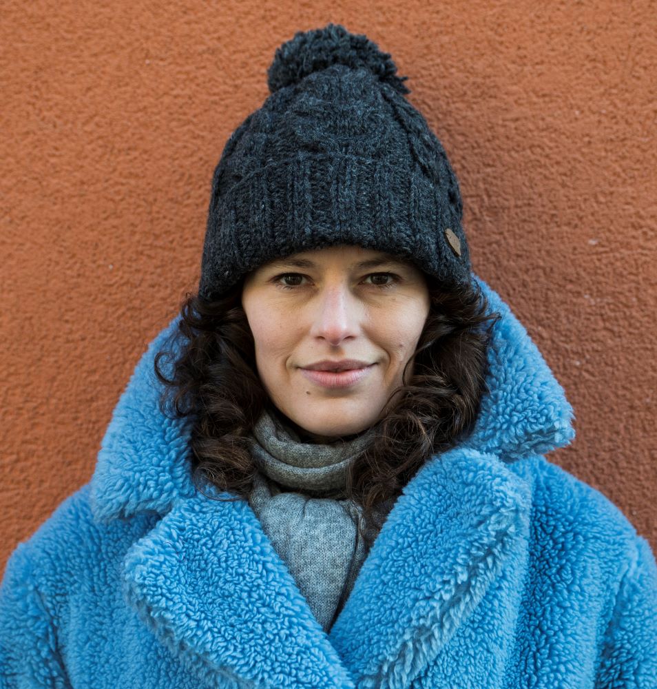 A woman wearing a dark gray cable-knit beanie with a pom-pom 