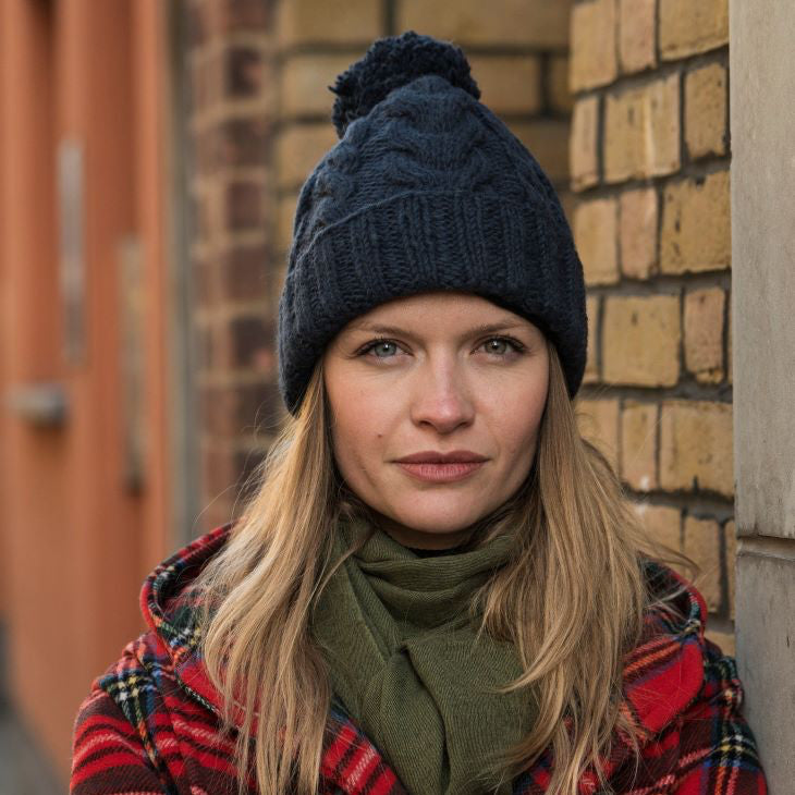 A woman wearing a dark navy blue cable-knit beanie with a pom-pom by KuSan
