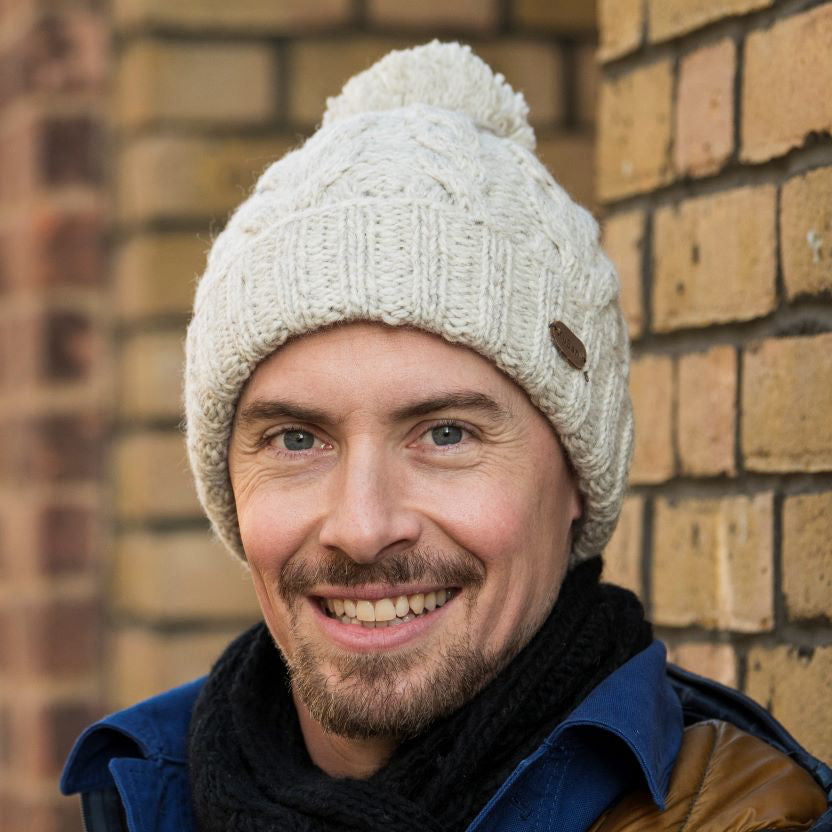 A smiling man wearing a cream cable-knit beanie with a pom-pom by KuSan