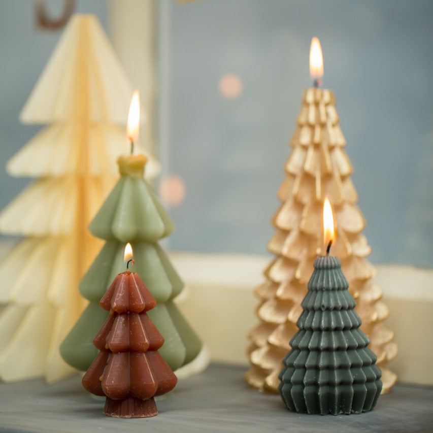 Three Christmas tree-shaped candles with lit flames, including a dark green textured tree, a light green tree, and a gold tree