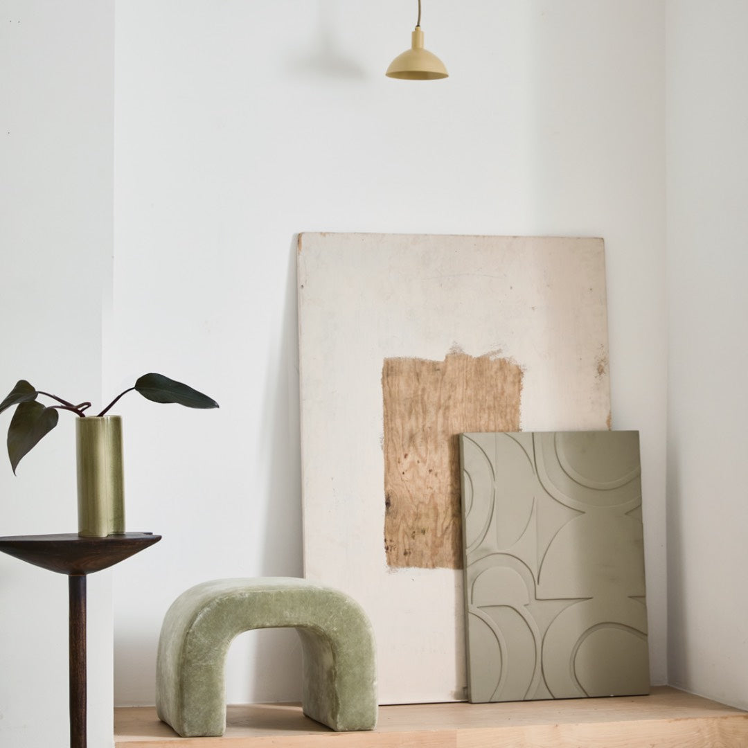 Modern interior with a green stool, plant, and abstract art on a white wall.