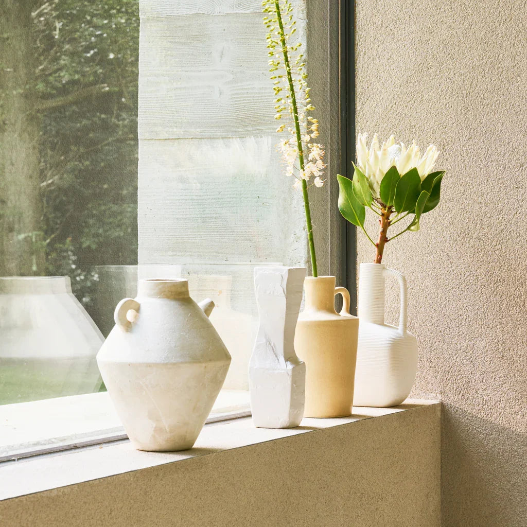 Collection of white and beige vases with plants on a windowsill.