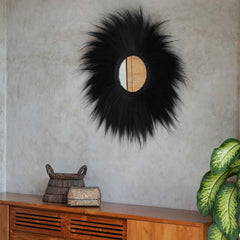 Decorative black mirror with fluffy texture on a gray wall above a wooden console table.