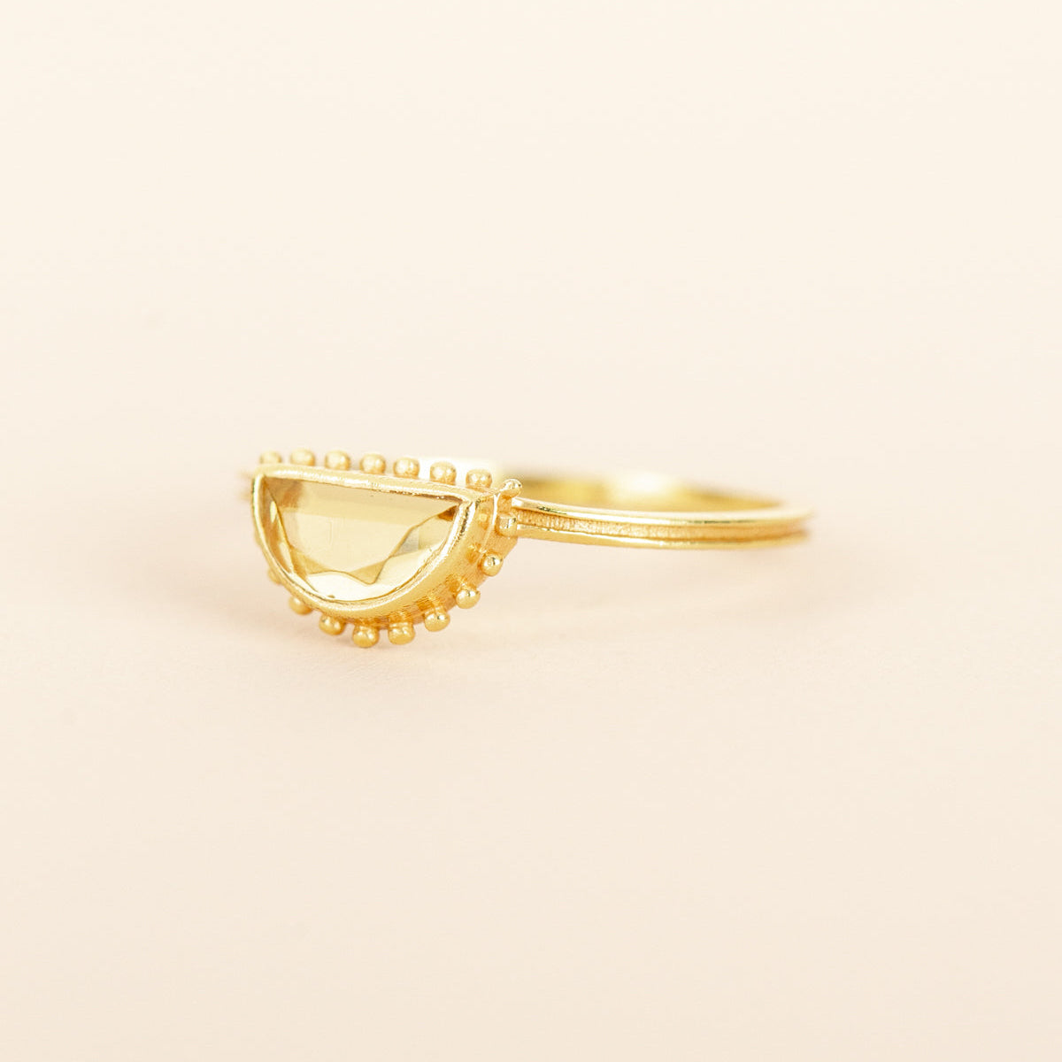 A gold ring with a semi-circular, beaded halo setting holding a pale yellow citrine gemstone
