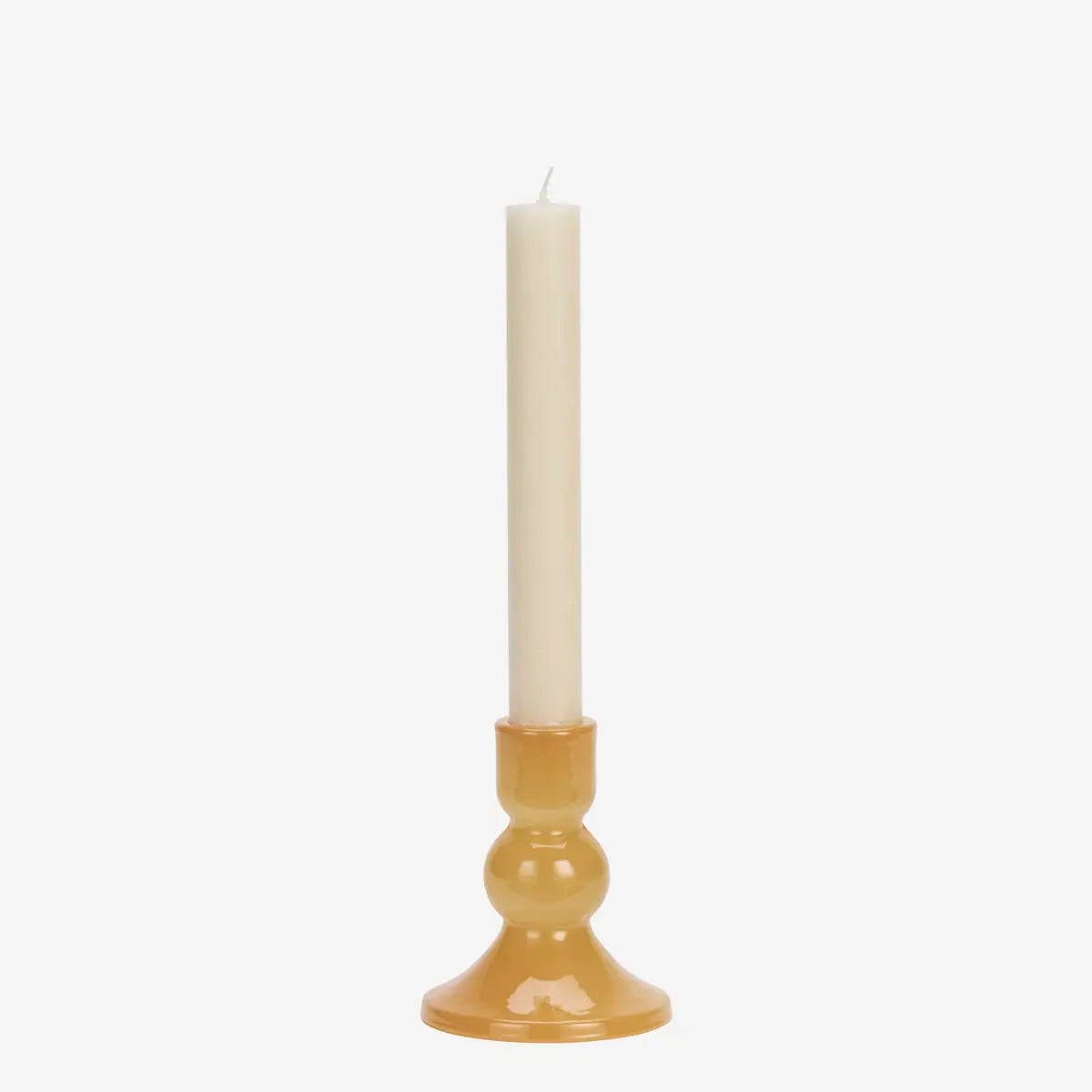 A single cream taper candle standing upright in a glossy amber glass candlestick holder