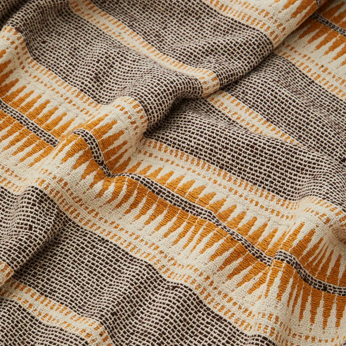 A close-up of a woven textile with a striped pattern in dark brown, cream, and mustard yellow, showing the detailed texture of the fabric.
