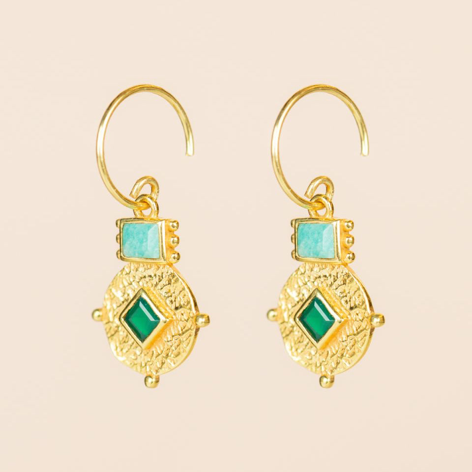 Gold earrings with green gemstones on a beige background Mujajuma