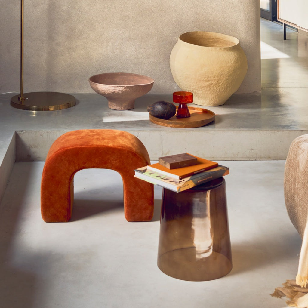 Modern interior with orange stool, metallic table, and decorative items on a light gray floor.