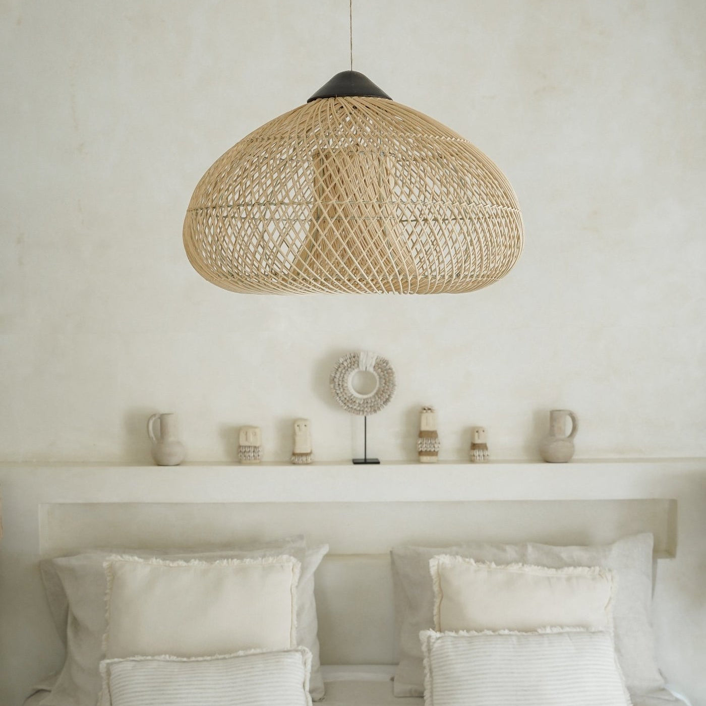 Woven pendant light over a bed with white bedding and pillows in a minimalistic room.
