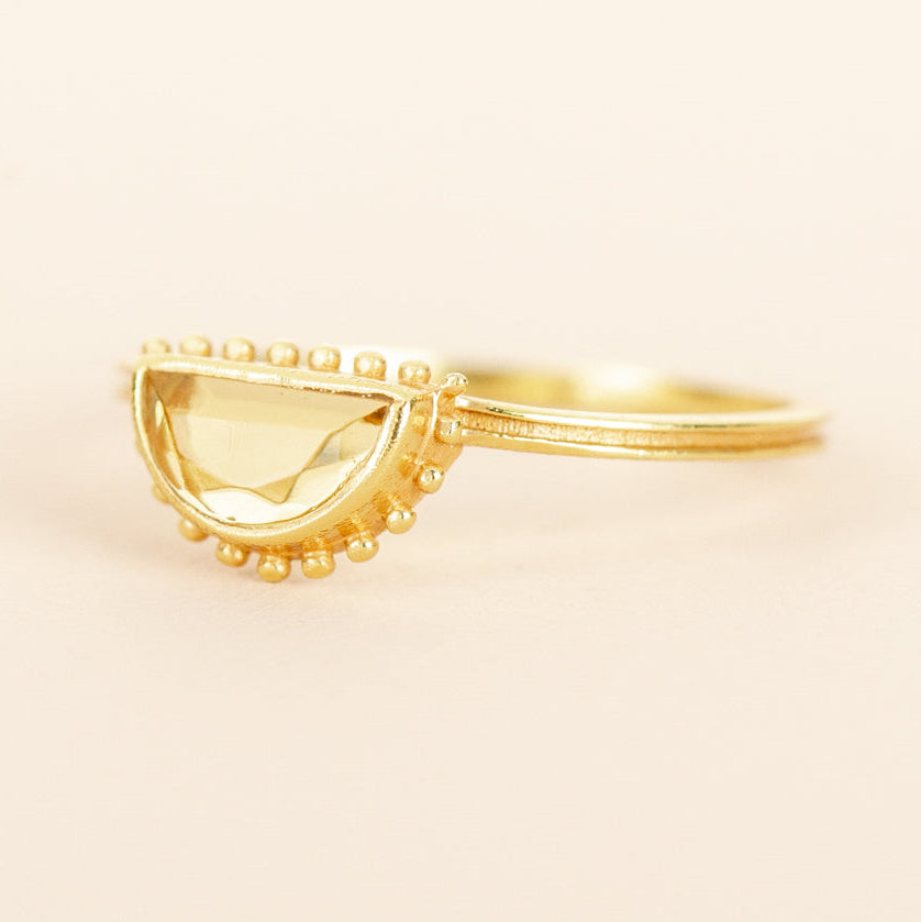 A gold ring with a semi-circular, beaded halo setting holding a pale yellow citrine gemstone Muja Juma.