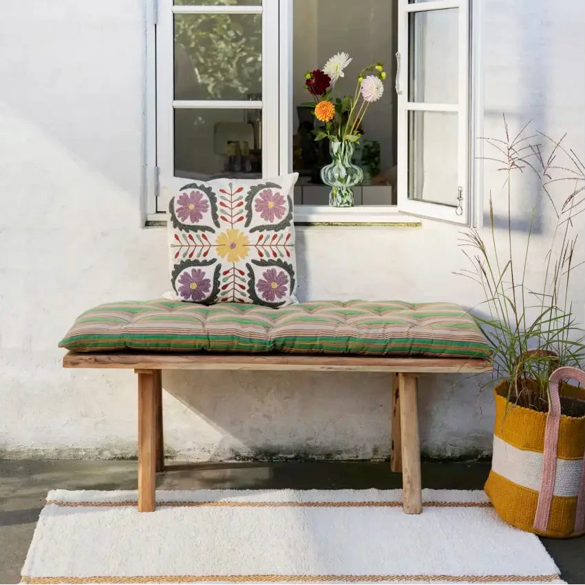 Wooden bench with embroidered cushion in front of a window with open shutters.