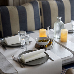 Dining table setting with plates, glasses, and candles on a striped cushioned bench.